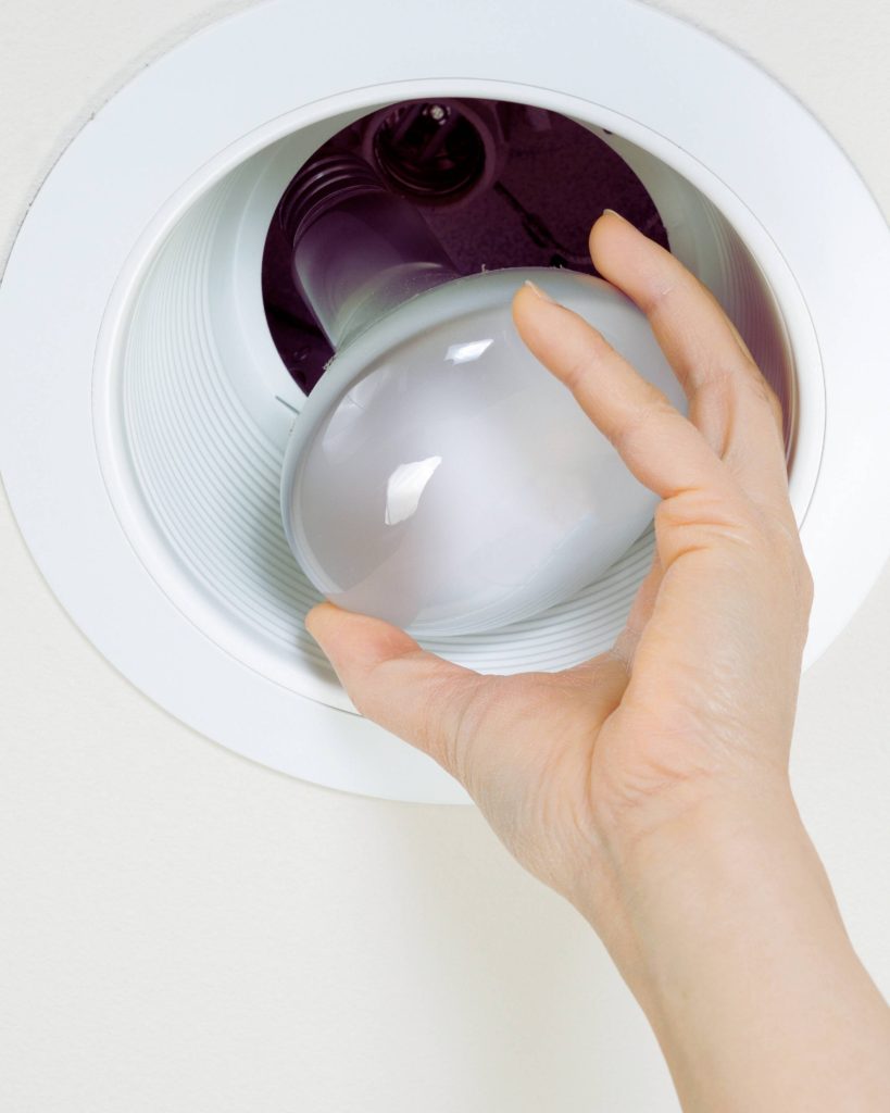 Hand removing an old recessed can light bulb during LED retrofit installation