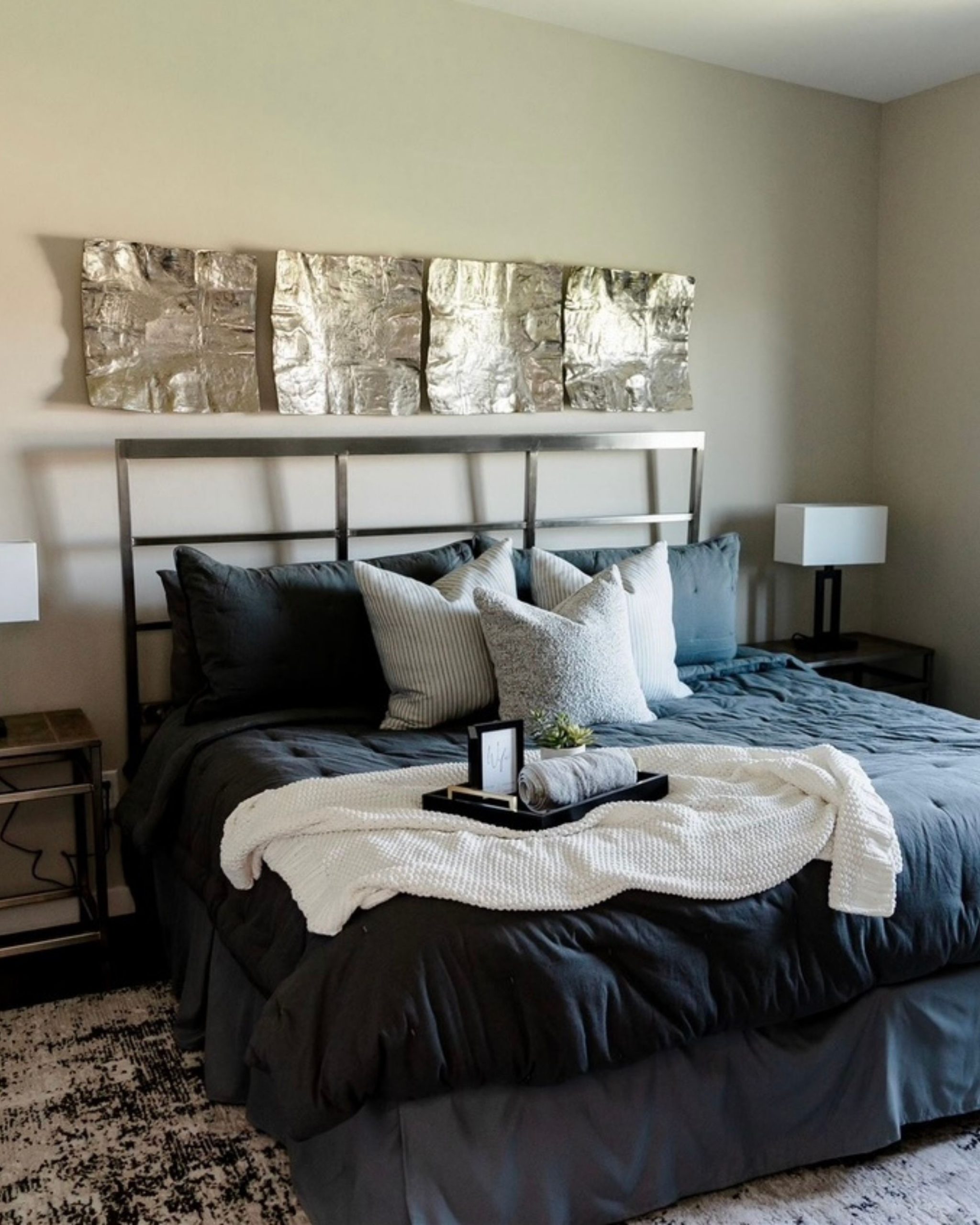 Hotel-style guest bedroom with layered neutral bedding, accent pillows, and a welcoming tray on the bed
