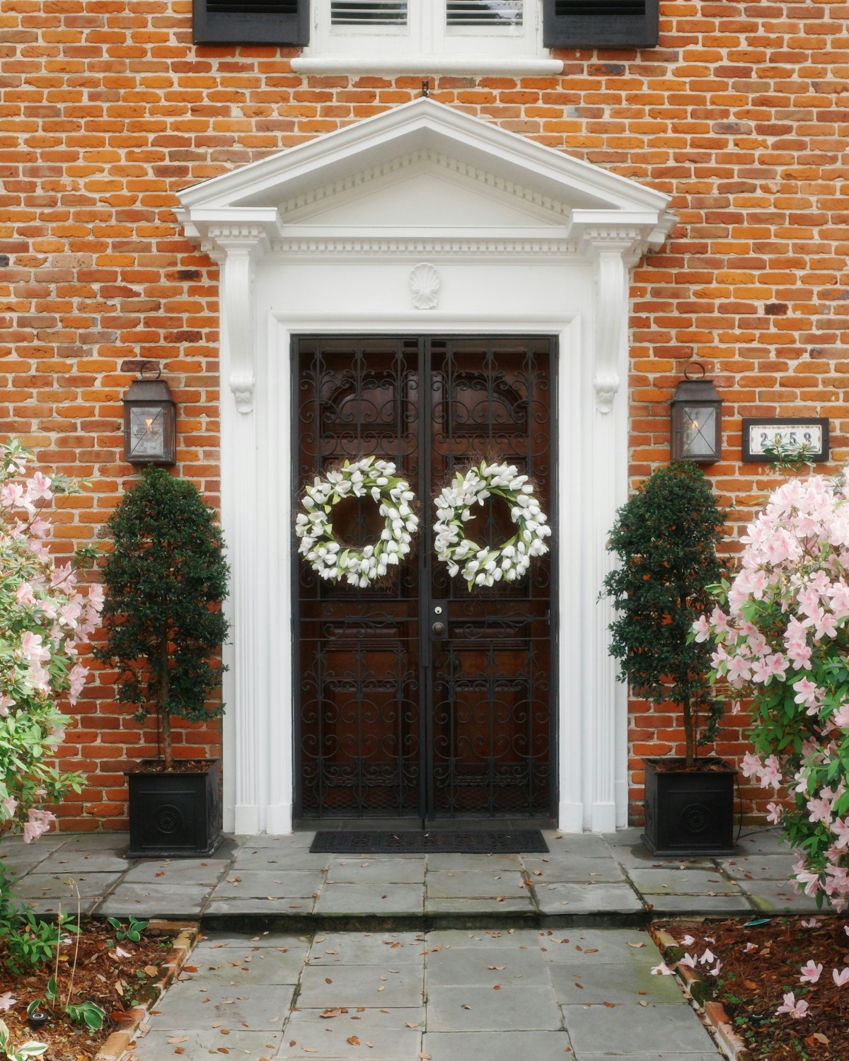 front porch with faux outdoor plants in black planters flanking double doors with white wreaths