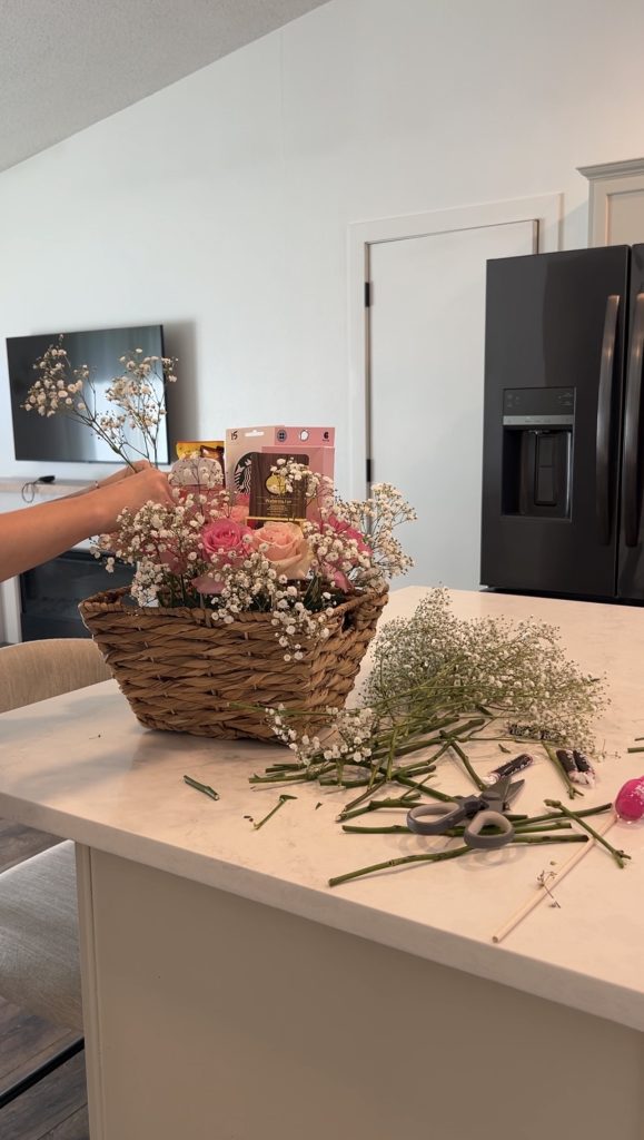 Adding baby’s breath and pink roses around gift items in a woven basket to create a finished DIY bloom basket centerpiece.