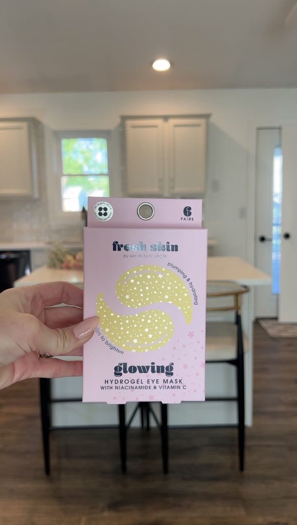 Hand holding pink hydrogel eye mask packaging used as a self-care item in a DIY bloom basket.