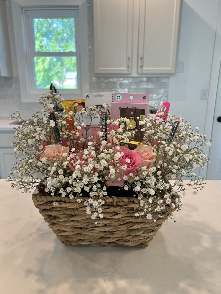 Finished bloom basket arrangement with pink roses, baby’s breath, self-care products, candy, and a Starbucks gift card styled inside a woven wicker basket.