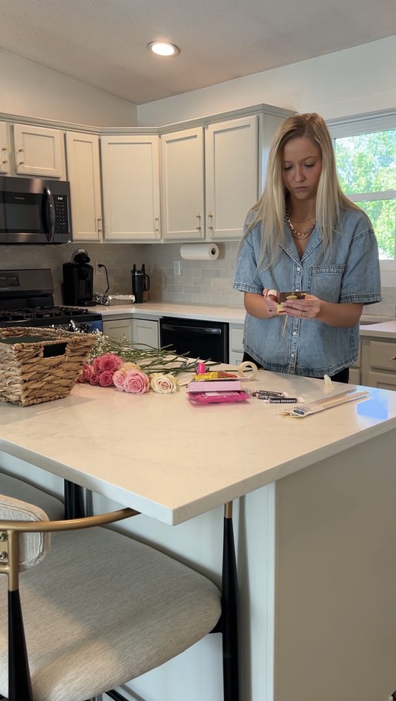 Arranging gift basket supplies including flowers, beauty products, candy, and skewers before creating a bloom basket arrangement.