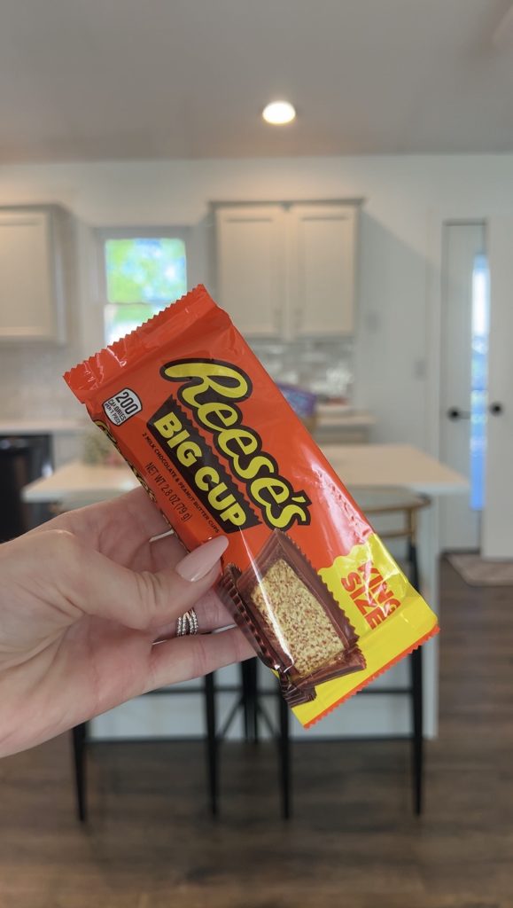 Hand holding Reese’s Big Cup king size peanut butter cups as a sweet treat for a bloom basket gift arrangement.