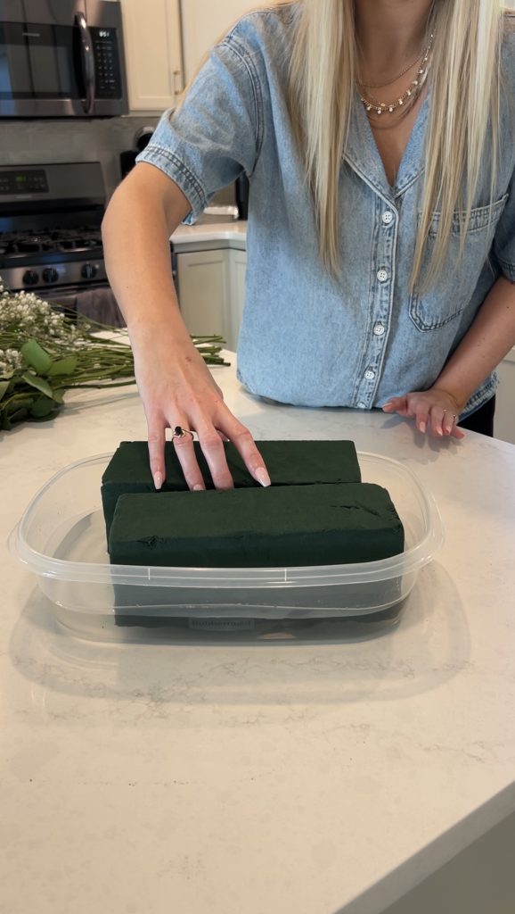 Soaking floral foam bricks in water inside a plastic container before assembling a fresh flower bloom basket.