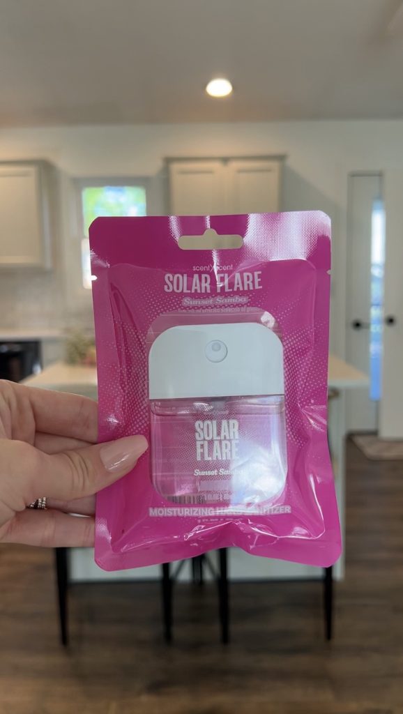 Hand holding a pink Solar Flare Sunset Sorbet air freshener in front of a kitchen background.