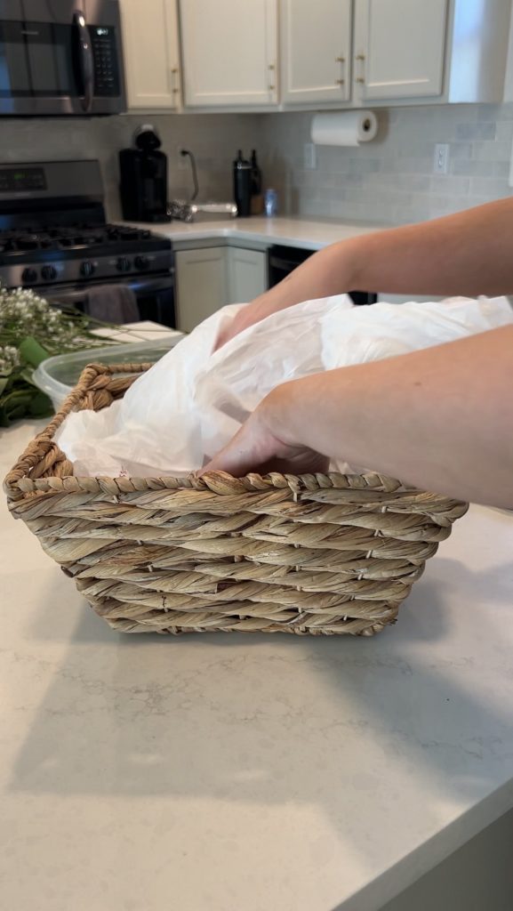 Lining a woven wicker basket with a plastic bag before adding floral foam for a DIY bloom basket arrangement.
